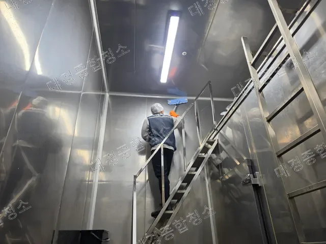 사다리 위에서 밀대로 벽면을 청소하는 작업자